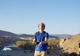 Wearing a blue shirt and a backpack, Ryan Ozminkowski looks up as he juggles rocks. A canyon is in the background.