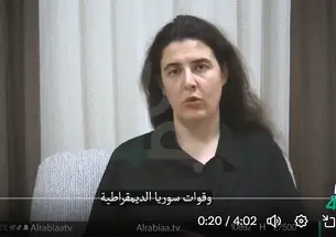 Elizabeth Tsurkov speaks in front of a curtain, wearing a black collared shirt.