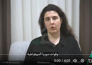 Elizabeth Tsurkov speaks in front of a curtain, wearing a black collared shirt.