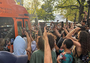 Protesters surrounding a University bus, holding up cell phone cameras