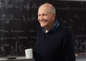 This is a photo of Frank N. von Hippel in front of a chalkboard. He's holding a coffee mug.