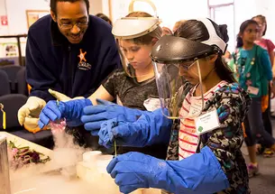 Atiba Brereton, a diagnostic engineer at PPPL, looks on as Mackenzie Keane, left, a fourth grader from East Brunswick, N.J., and Shreya Joshi, a fifth grader from West Windsor, N.J., try their hands at a cryogenics experiment at PPPL. (Courtesy Elle Stark
