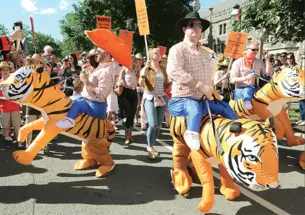 This is a photo from the P-rade in 2017 of the Class of 2002 riding inflatable tigers. One is wearing an orange cowboy hat.