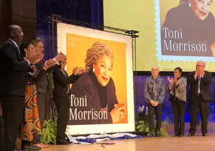 Seven people stand next to a large poster of a postage stamp featuring Toni Morrison