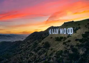 The sun sets behind the famous HOLLYWOOD sign on a hill in California.