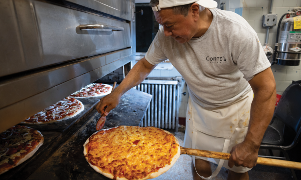A cook at Conte's pulls a pizza out of the oven.