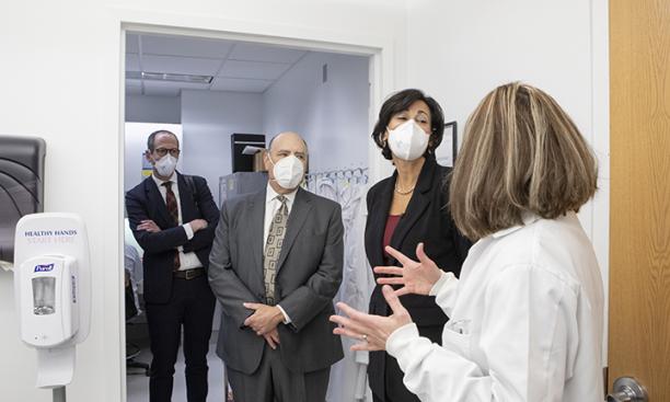 This is a photo of Rochelle Walensky wearing a white face mask and speaking with a woman in a lab coat. Two men also in white face masks stand behind Walensky.