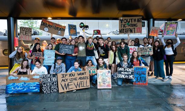 Princeton students holding signs to protest the use of fossil fuels are posed on a train platform