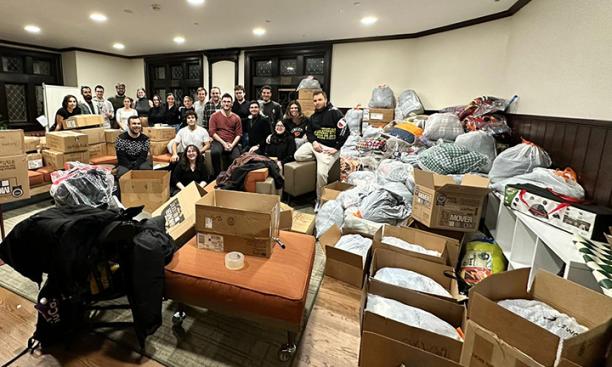 About 20 people pose in a room full of boxes and bags of donated supplies.
