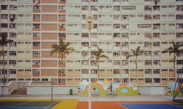 Brightly colored tennis courts are separated by a row of palm trees from two rainbow murals and an apartment building.
