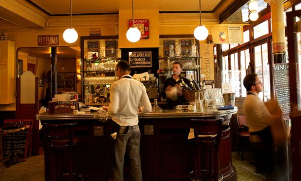 A waiter stands at a bar under three pendant lights.