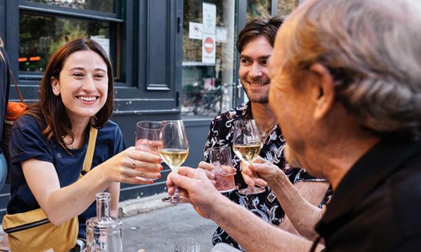 Three people clink glasses at an outdoor table in Paris.