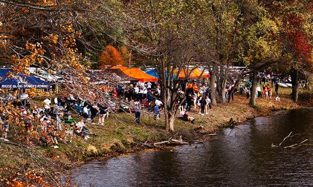 The photo shows spectators on the side of Lake Carnegie, and a line of orange and blue tents.