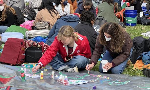 Two women paint a banner on the ground.