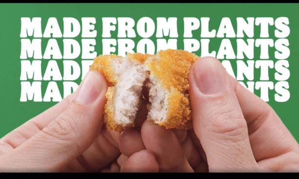 Fingers break open a vegan chicken nugget with the words "Made from plants" in the background.
