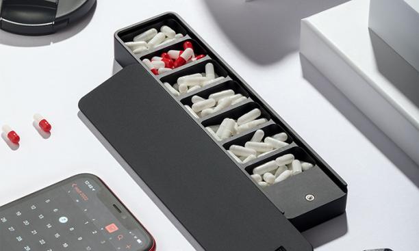 A dark gray pill case with seven compartments in a line and the lid off.