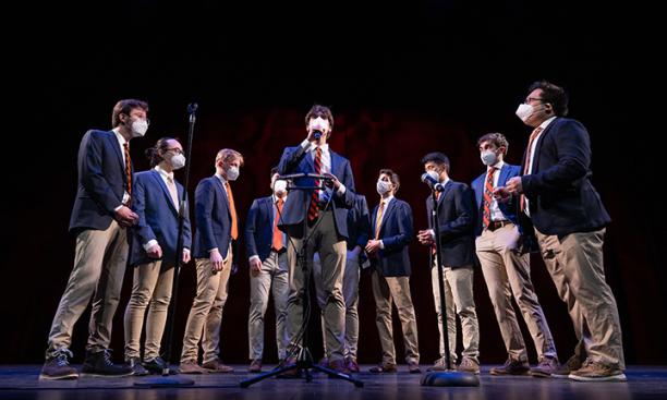 Ten singers in the Tigertones stand in a half circle singing on a stage, wearing blue blazers and khakis