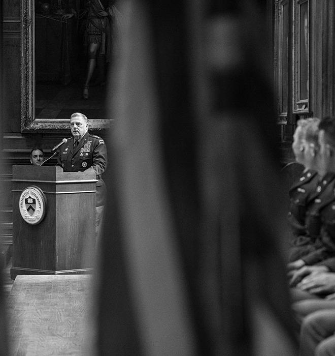 In this black and white photo, Gen. Mark Milley speaks at a podium on the left bearing the Princeton seal, while young men in military uniforms watch him from the right.