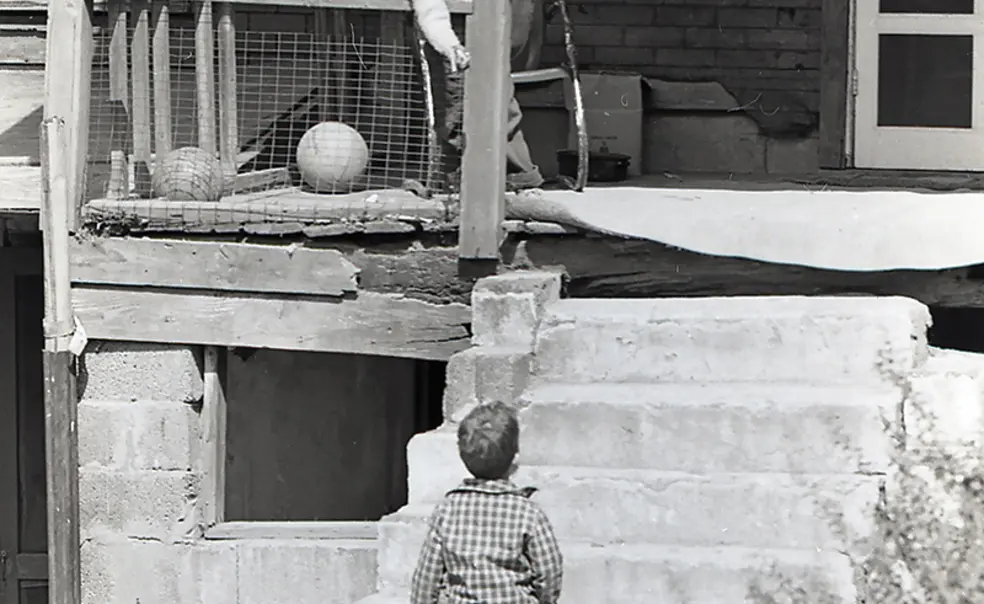 PRINCE_060-Siegel-003 copy.jpg In this black-and-white photo from the 1960s, a boy stands on the porch of a home in rough shape, talking to another boy on the ground.