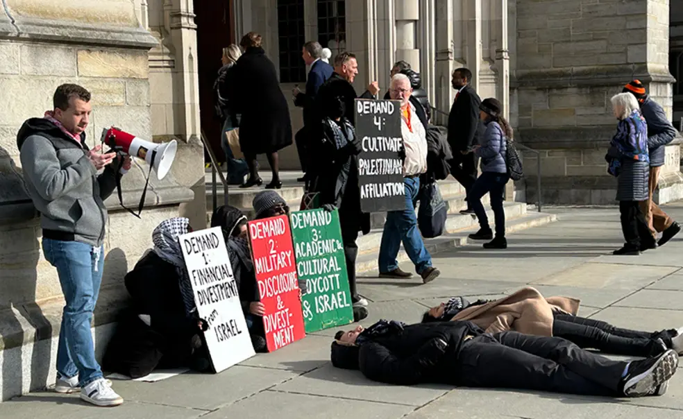 Palestinian_protest_alumni_day_2025.jpg People walk into the Princeton chapel past a pro-Palestinian protest where two people are laying on the ground.
