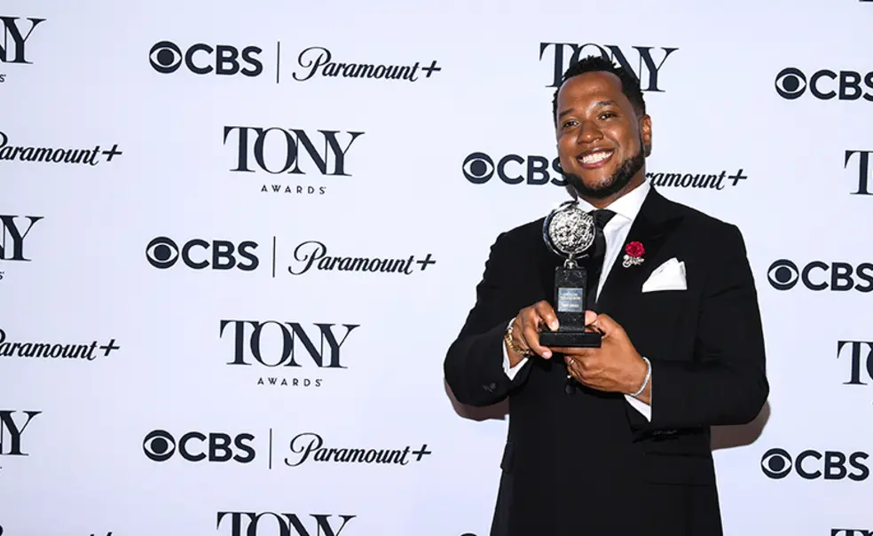 Branden Jacobs-Jenkins ’06 holds his Tony award in front of a step-and-repeat covered with logos for CBS, Paramount+, and the Tony Awards.