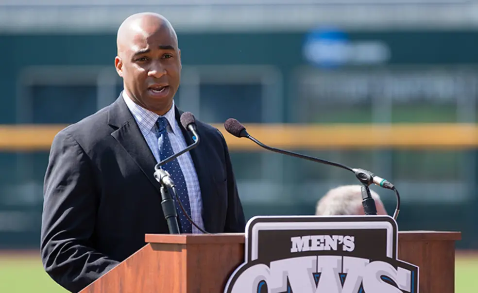AITN041222.jpg Damani Leech ’98 speaks at a podium with a baseball field in the background.