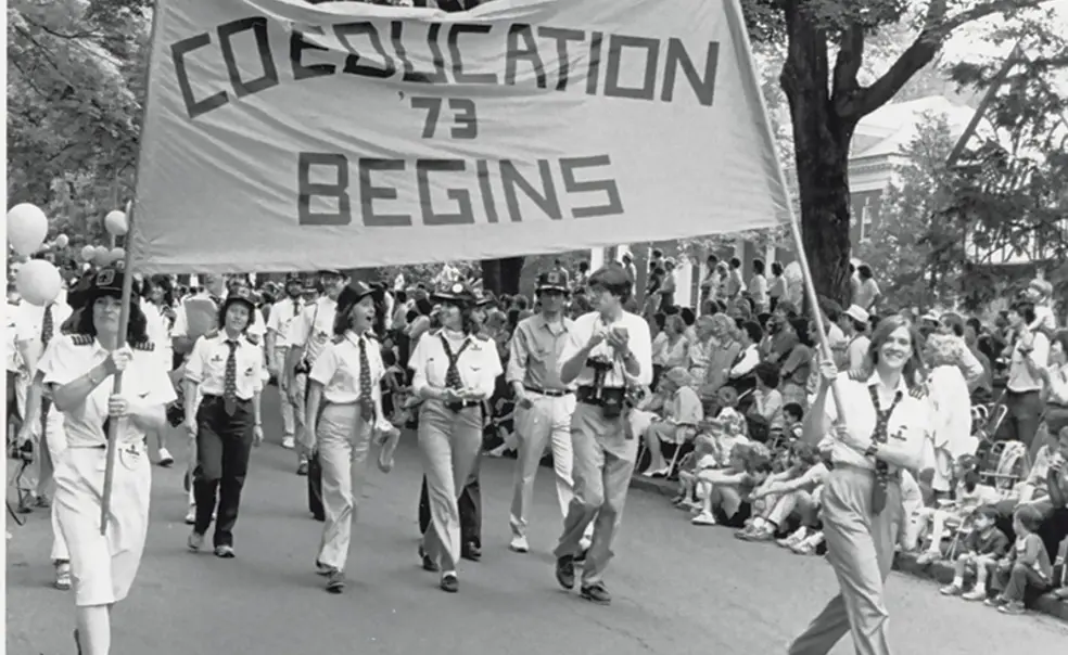 Co_Education begins 1983 P-rade.jpg The Class of ’73 marches proudly with the “Coeducation Begins” banner at Reunions in 1983.