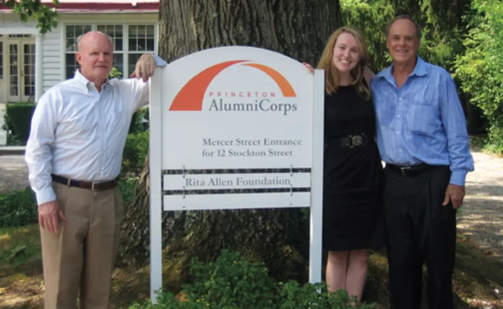 LIVE.AS_PP55.jpg  Standing next to the sign introducing Princeton AlumniCorps — formerly Princeton Project 55 — are, from left, president Bill Leahy ’66, executive director Kathleen Reilly, and board chairman Kenly Webster ’55.