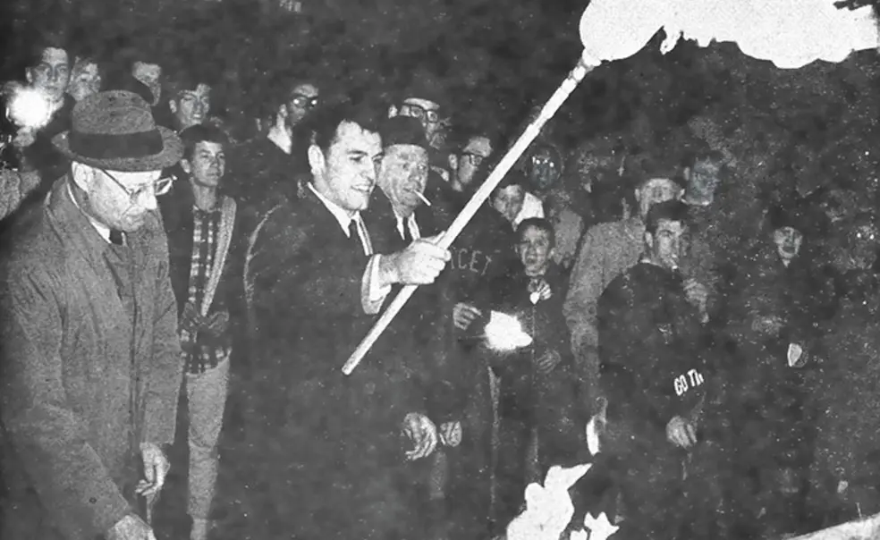 TWT1-Anew.jpg All-American Cosmo Iacavazzi ’65 *68 lights the bonfire, with coach Dick Colman (in glasses) by his side.
