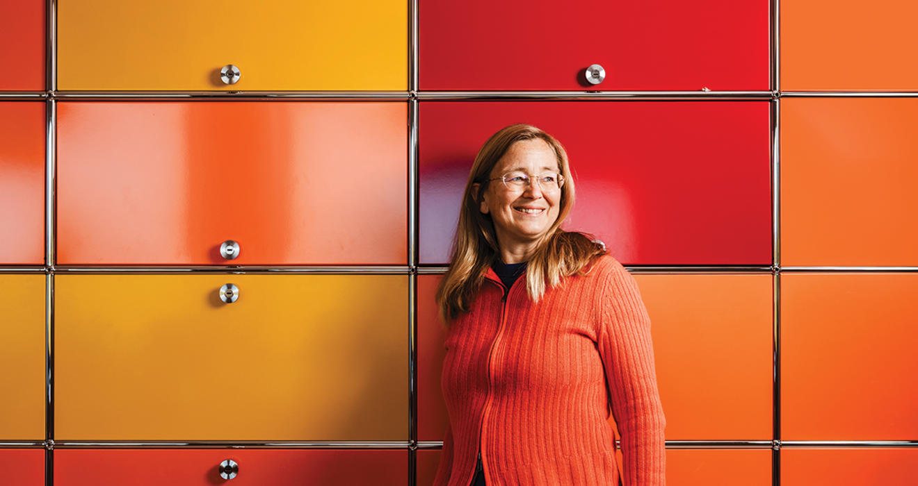 Kim Scott stands against a wall of yellow, orange, and red cabinets.