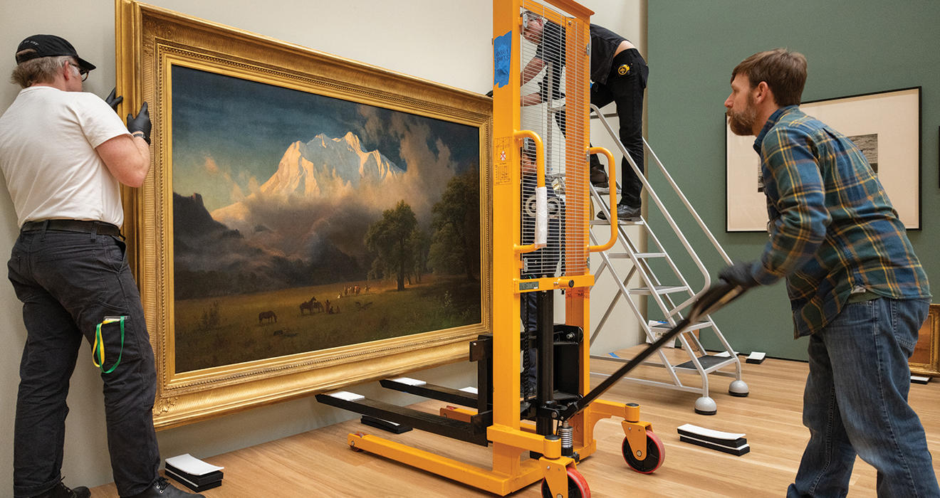 Two men move a large painting of a landscape into the new art museum. 