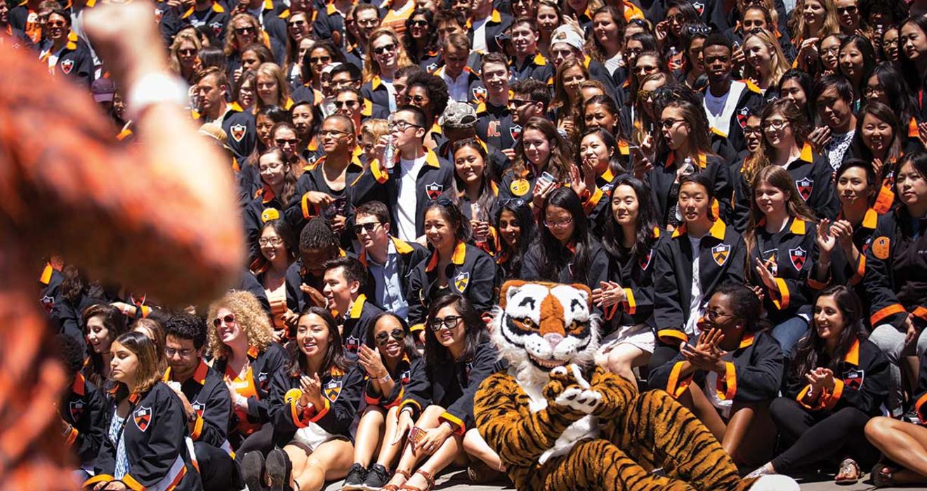 The Class of 2017 gathers in their black jackets behind the Tiger mascot, who's sitting on the ground and clapping his paws.