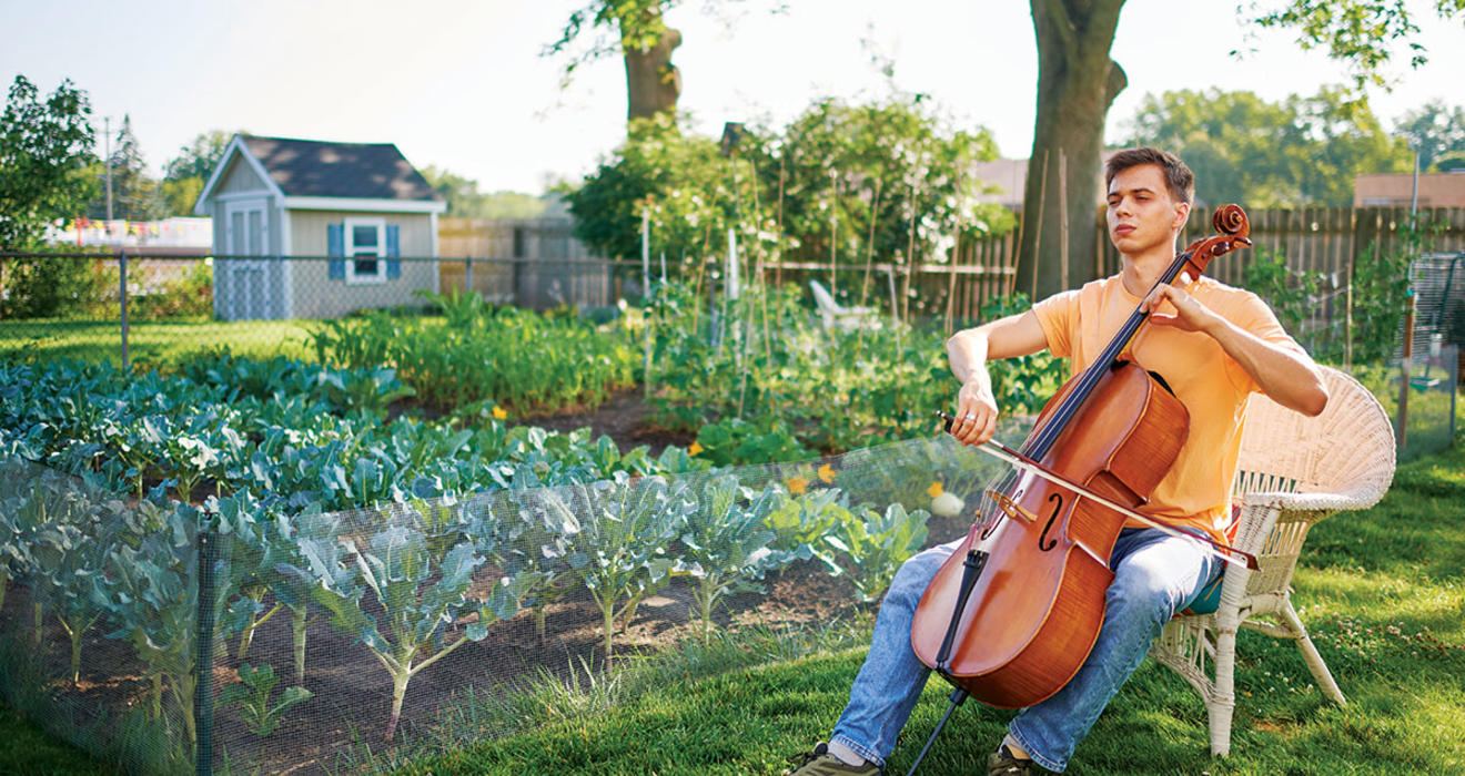 With his eyes shut, Calvin Van Zytveld ’19 plays a cello outdoors, a garden and a shed in the background.