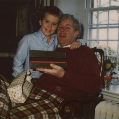 A boy wraps his arm around his dad's neck as both pose for a photo.