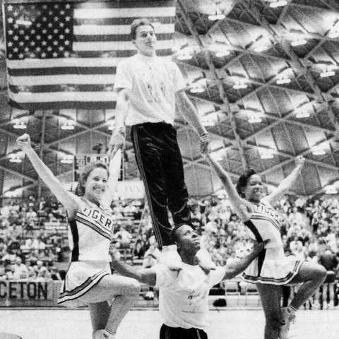 Four cheerleaders performing a lift on the sideline at a basketball game