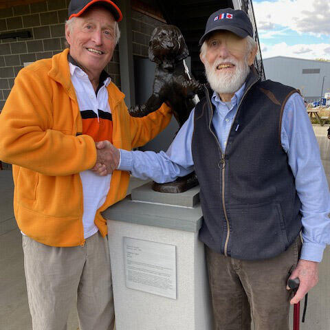 Two men shaking hands in front of a tiger statue