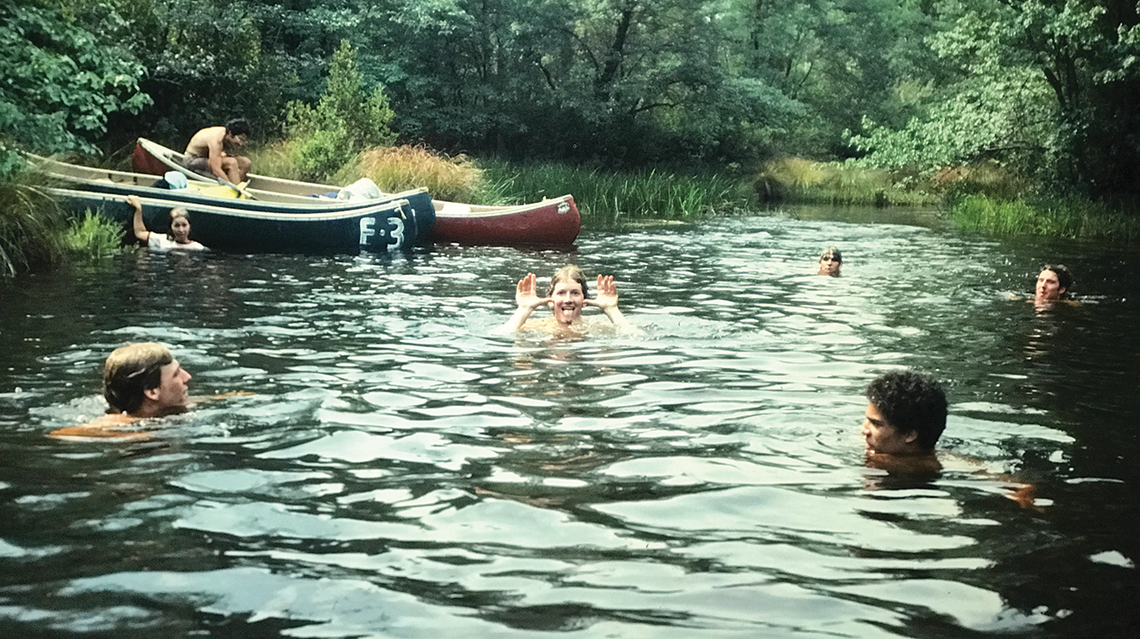 Students swimming in a river with canoes on the bank