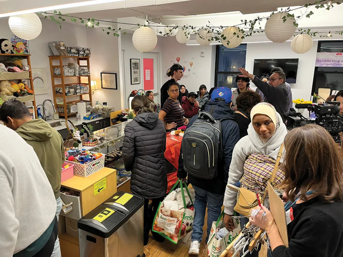 People pack into the Little Shop of Kindness; round paper lanterns and an ivy garland hang overhead.