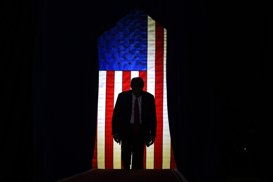 Trump standing in front of a lit U.S. flag surrounded by darkeness