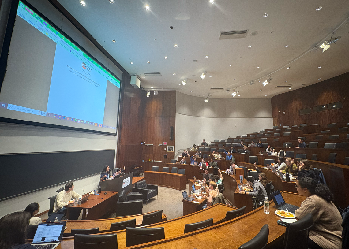 The USG meets in the Arthur Lewis Auditorium on Nov. 10. There is a document projected on the screen behind the USG Vice President. Members of the USG have their hands raised to vote.