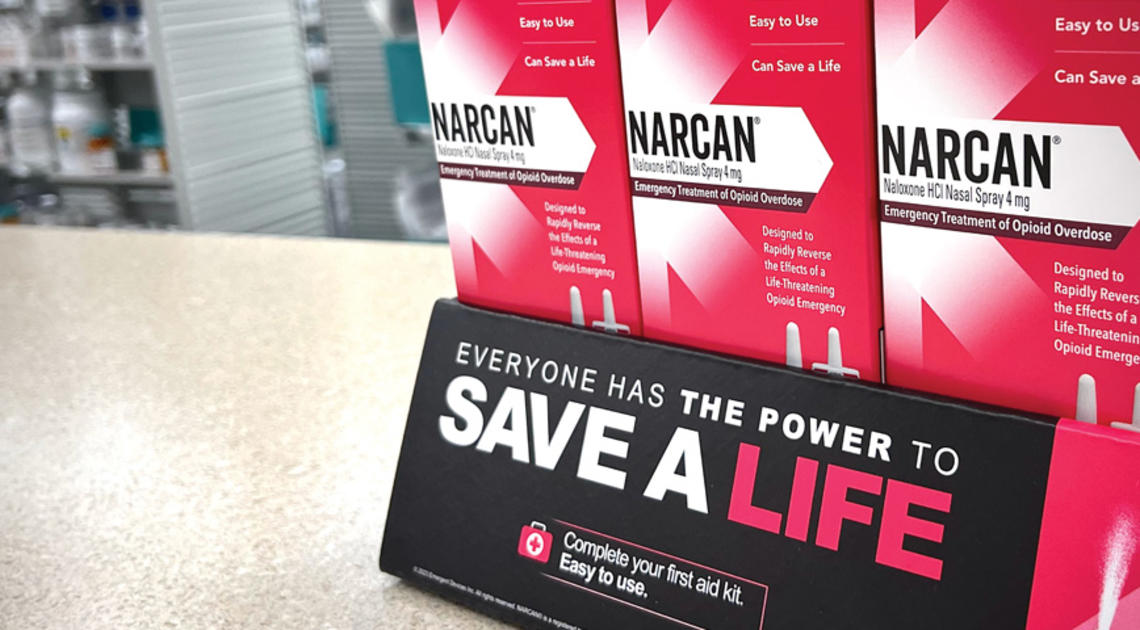 OTC_Narcan Student Overdoses Public Health.jpg Pink boxes of Narcan tacked on counter with a sign that reads Save a Life