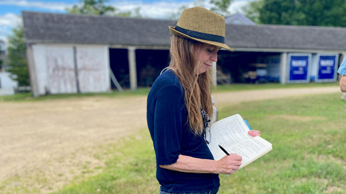 Michelle Lerner writes in a journal outdoors, a barn in the background.