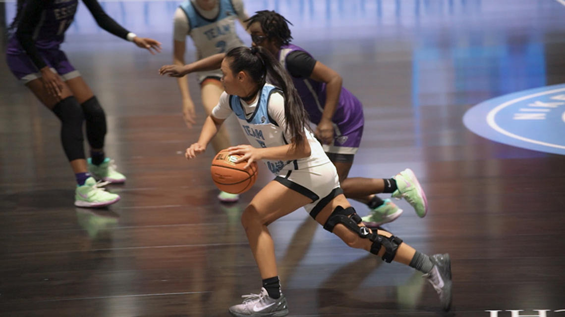 Ashley Chea ’27 dribbles down the court in her blue-and-white high school basketball uniform.