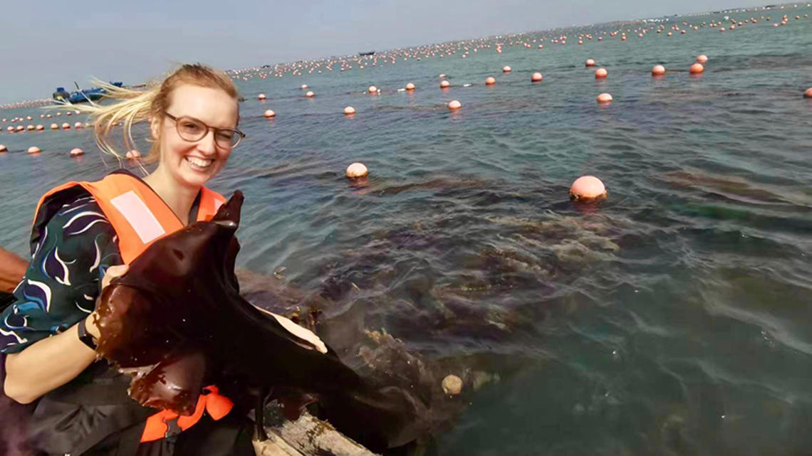 Helen Park sits in a boat holding a piece of kelp.