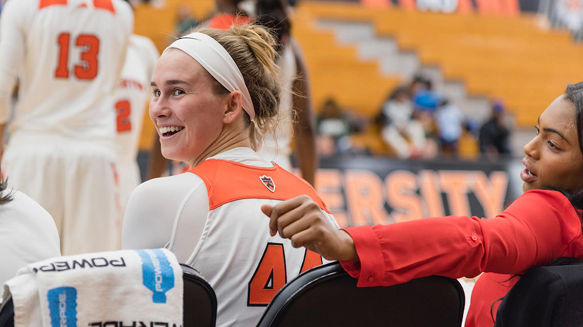 A Princeton basketball player smiles as she looks behind her from the bench on the side of a game.