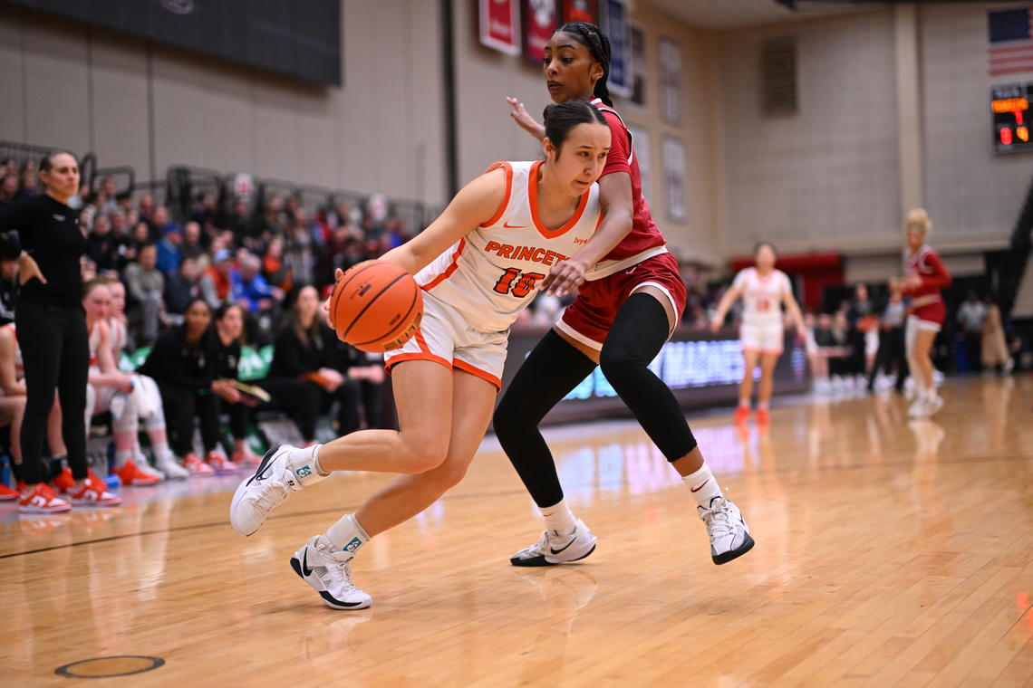 A Princeton basketball player dribbles inside, guarded tightly by a Harvard player. 