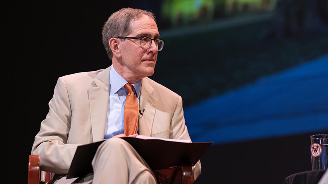 Princeton President Christopher Eisgruber ’83 holds an open binder on a stage.