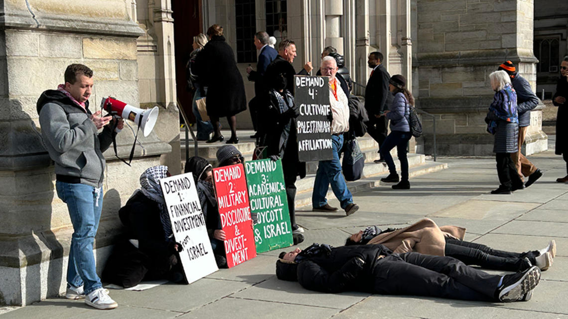 Palestinian_protest_alumni_day_2025.jpg People walk into the Princeton chapel past a pro-Palestinian protest where two people are laying on the ground.