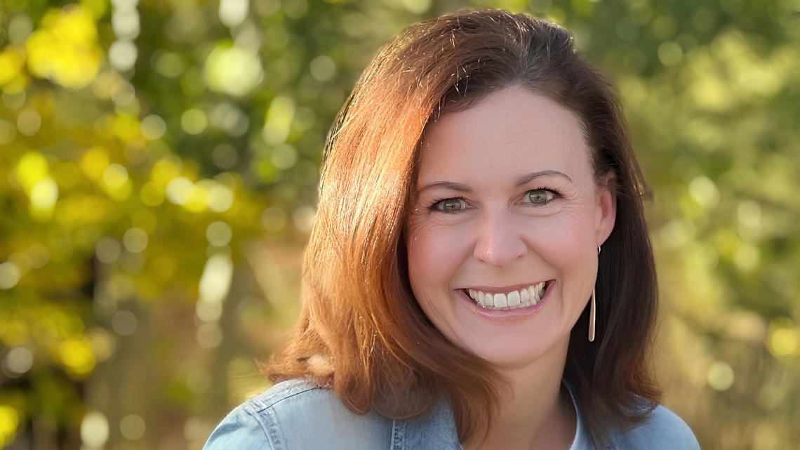 Andi Almond smiling for a photo with greenery in the background.