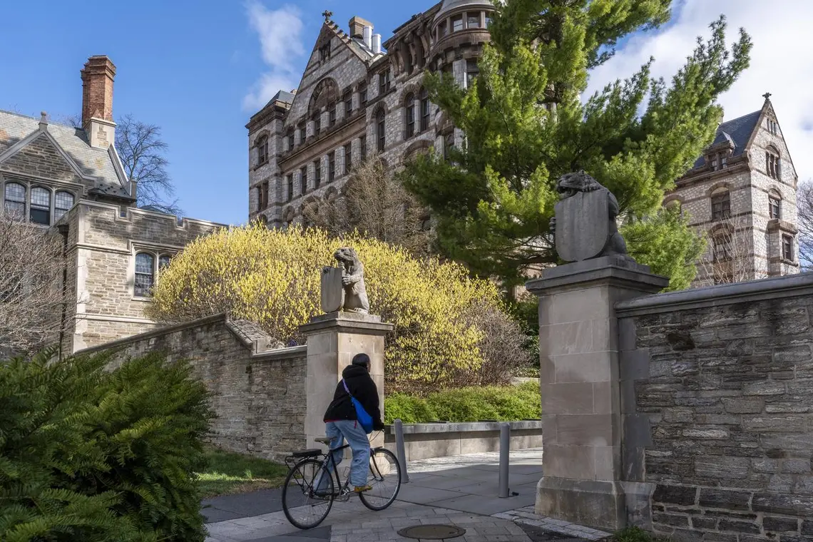 Bicyclist rides through a gateway flanked by two tiger statues holding shields